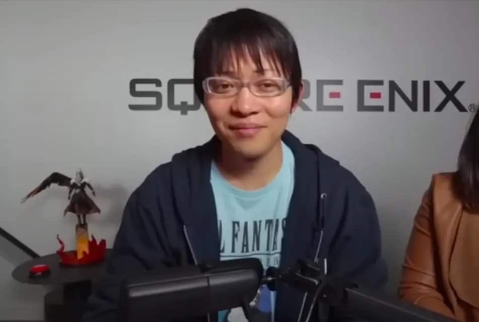 Naoki Hamaguchi mengenakan kacamata dan kaus biru, duduk di depan dinding berlogo Square Enix.